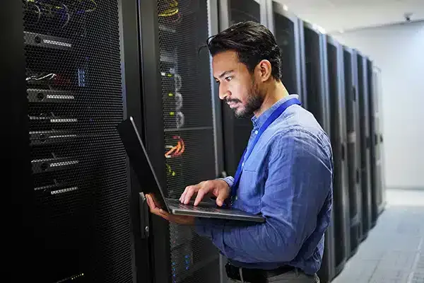 IT technician looking at laptop in front of servers.