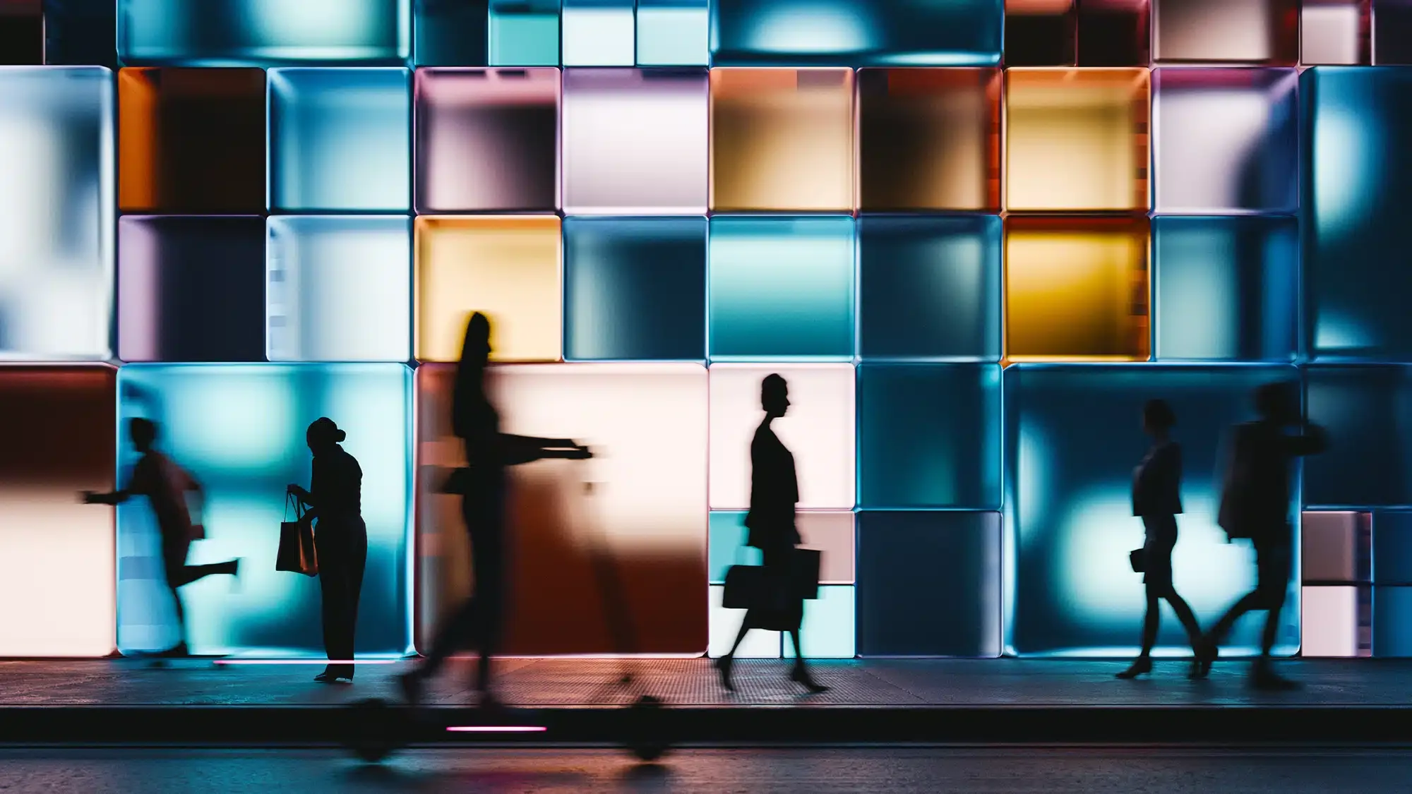 People walking behind colored wall.