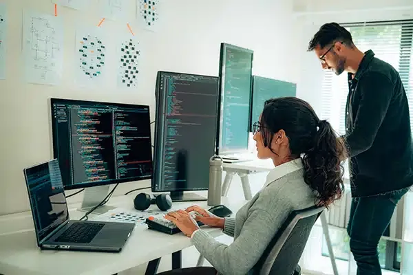 Woman sitting in front of computer system next to male IT tech standing in front of computer system in Denver, CO.