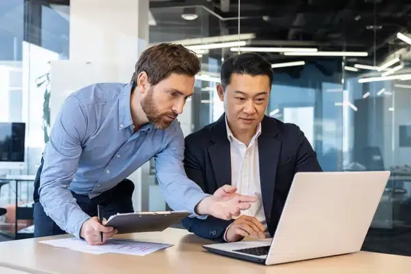 Manager training employee in front of laptop in office building.